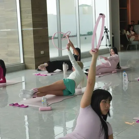 Una alumna sostiene un aro rosado de Pilates en alto durante una clase